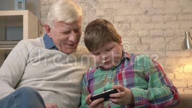 祖父和孙子坐在沙发上用智能手机，说着，一个胖孩子在玩智能手机